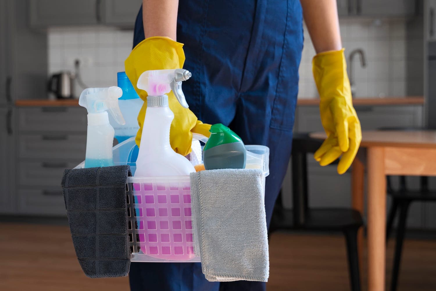 An OLAH Services team member in uniform and gloves carrying a stocked caddy of cleaning supplies